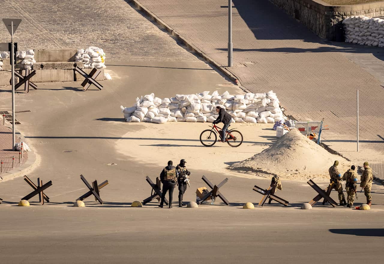 A cyclist rides past Ukrainian servicemen standing guard at a military checkpoint.