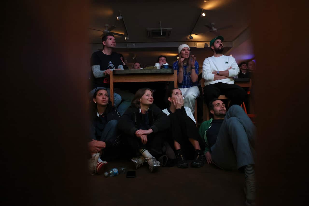 Football fans cover their faces as they watch the TV in a dark room.