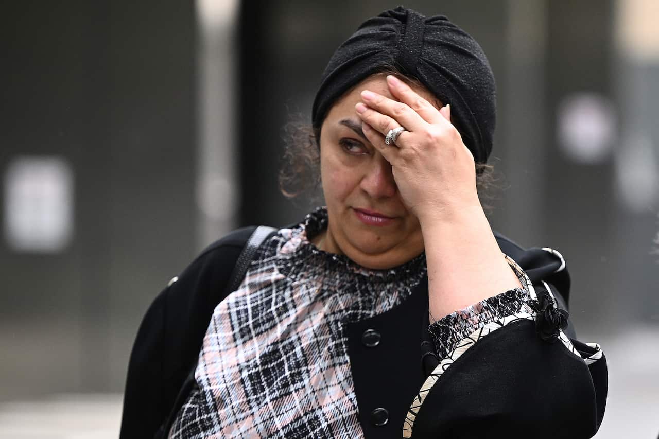 A woman partly covers her face with her hand while walking outside.