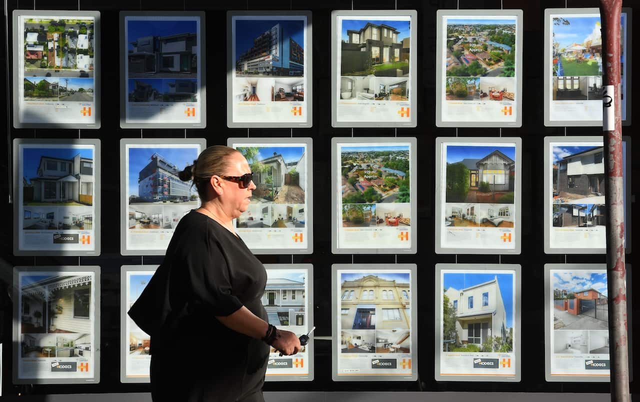 A woman walking past a window of real estate listings.