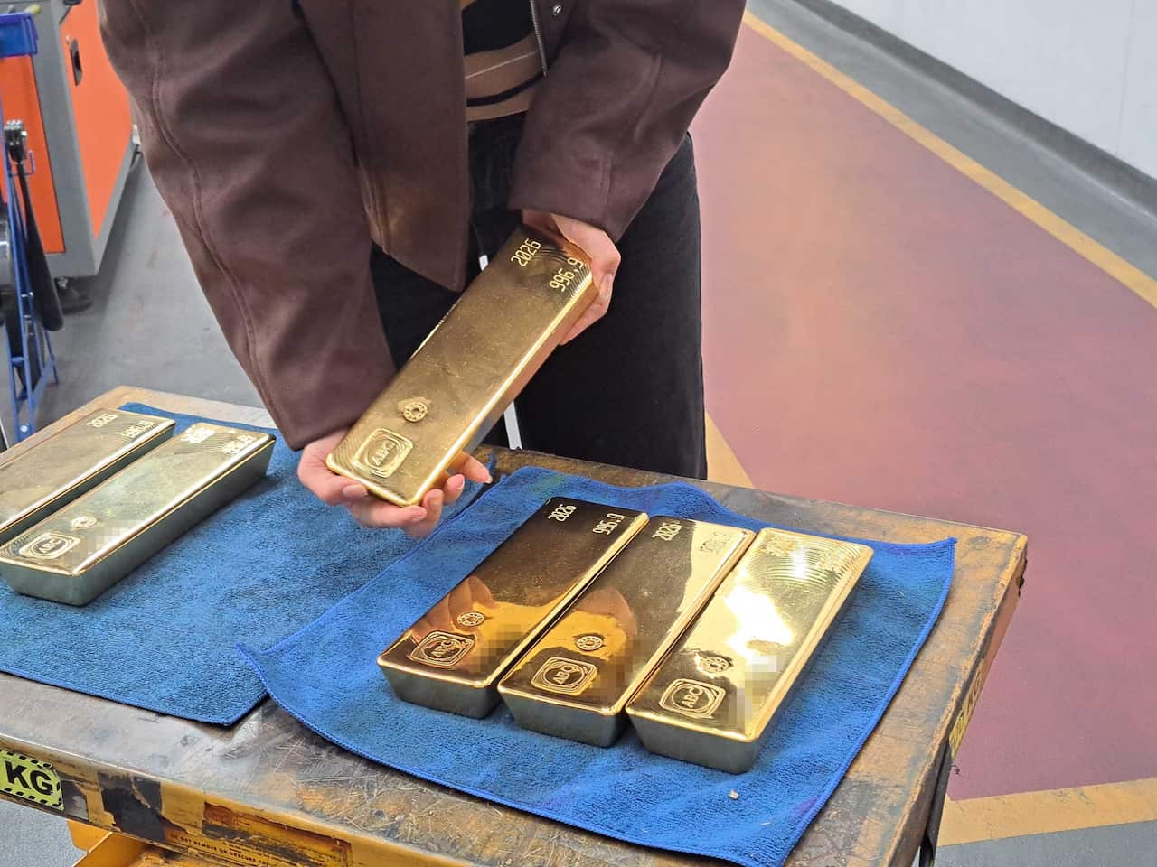 Someone holds a gold bar over a table with five other gold bars