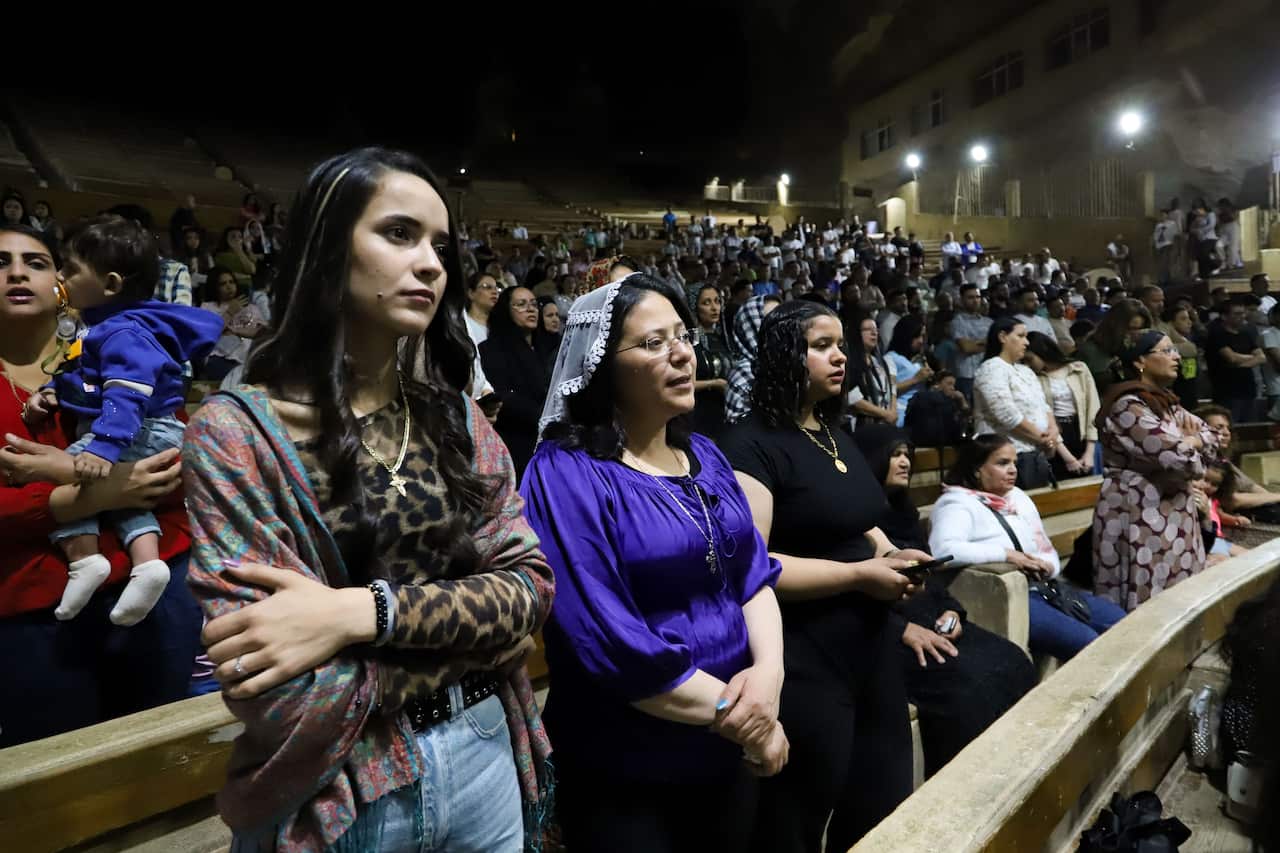 Several women stand in wooden pews looking forward with serious expressions.
