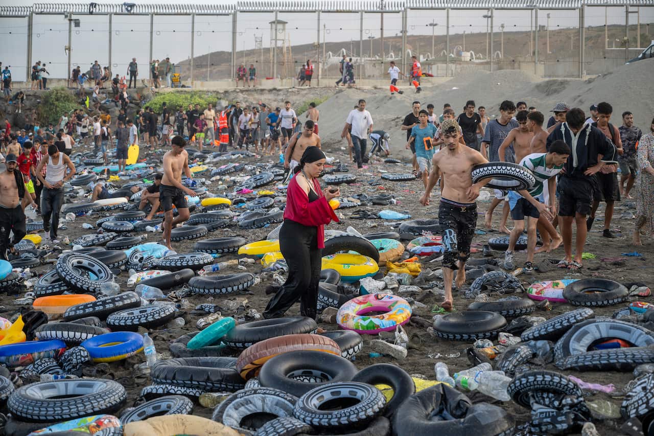 People walking on a beach covered with trash and rubber flotation rings.