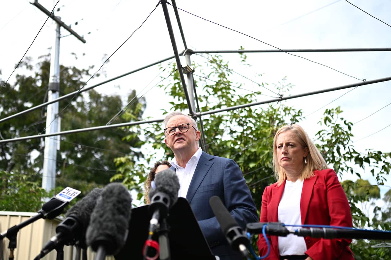 Anthony Albanese and Katy Gallagher in a backyard speaking in front of microphones.