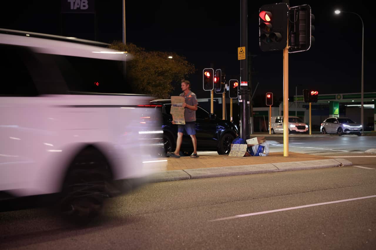 A man with cardboard sign at a busy intersection as cars go by