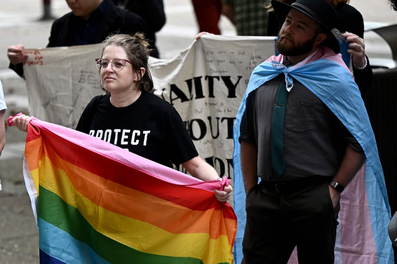 A woman stands outside the Federal Court in Sydney holding a rainbow flag.