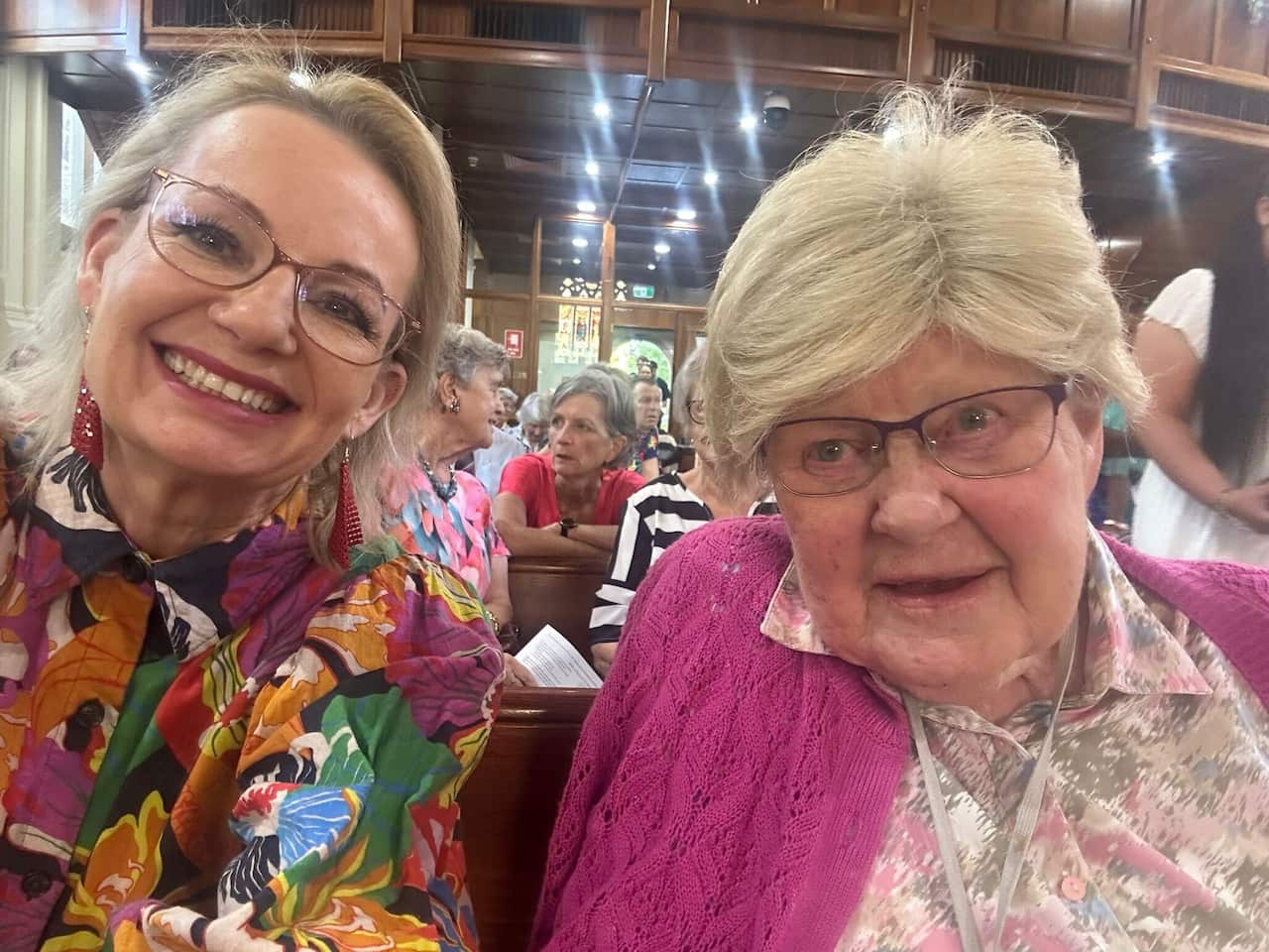 Sussan Ley in a floral shirt smiling, next to an older woman in a pink cardigan, who is also smiling.