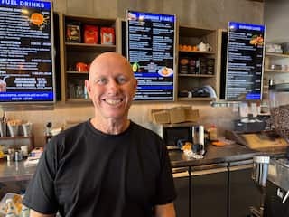 A man wearing a black t-shirt stands in front of a cafe menu