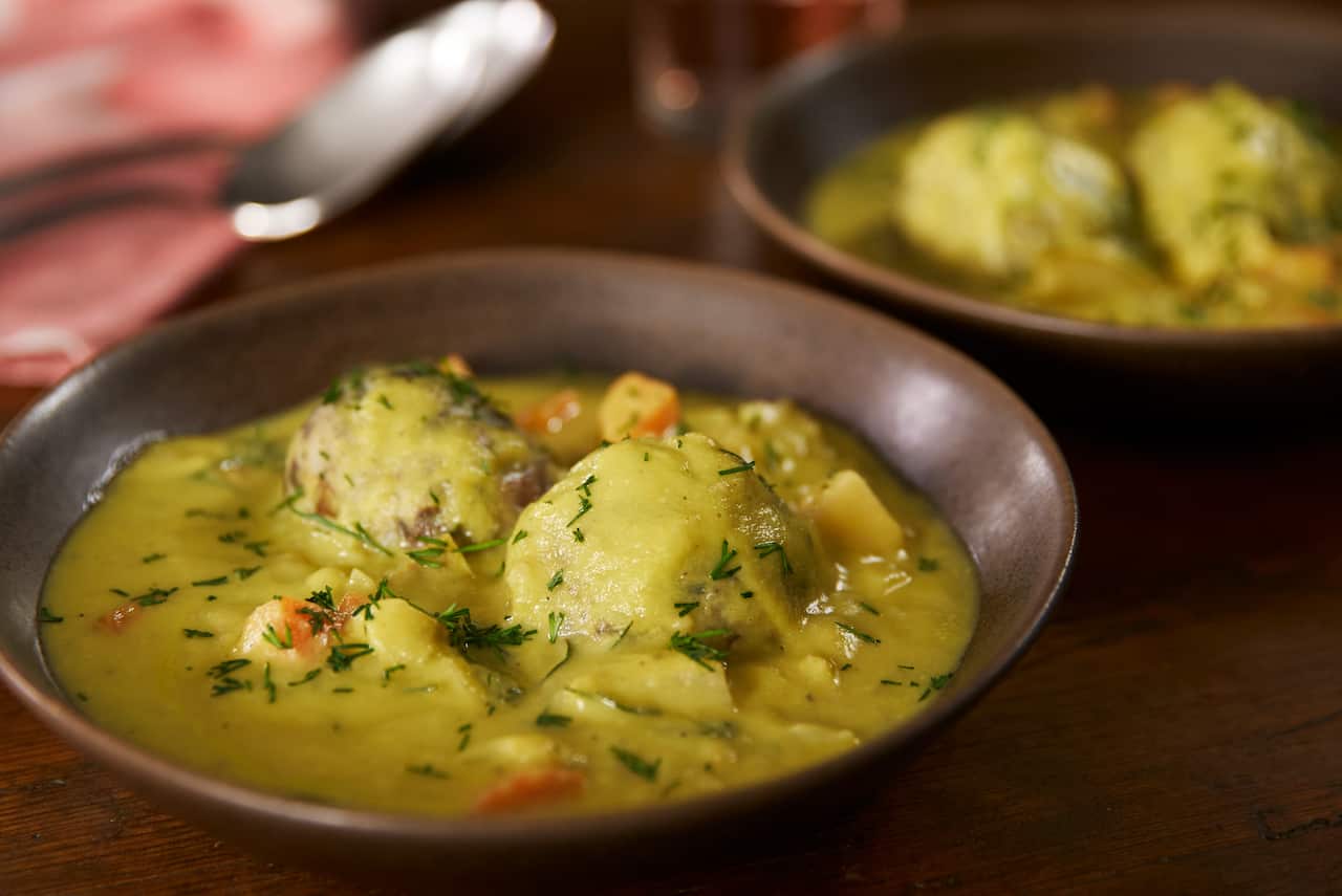 A wide browl bowl with a vibrant yellowish soup sits on a table, with a second bowl of soup behind it. 