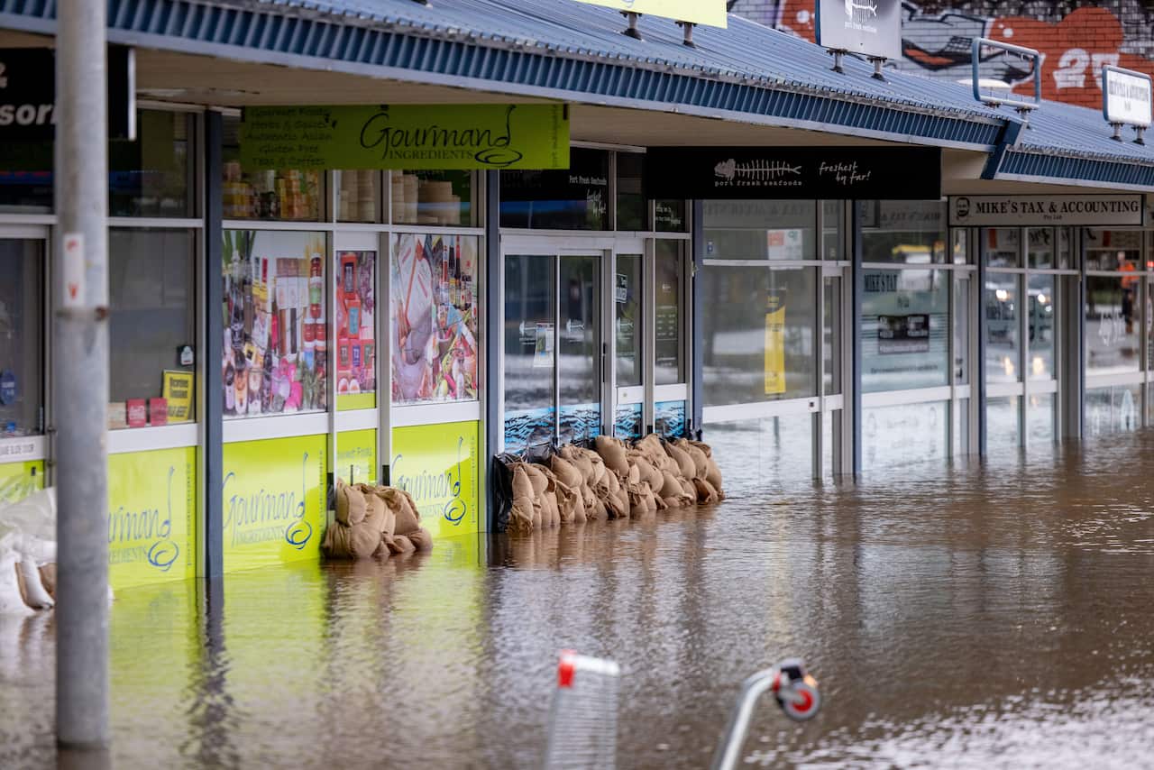 Sandbags in front of a green store, on a street inundated by brown floodwater.