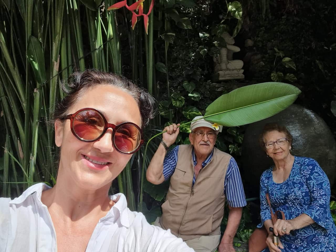 A woman in the foreground smiles, while her elderly parents sit behind her in the background.