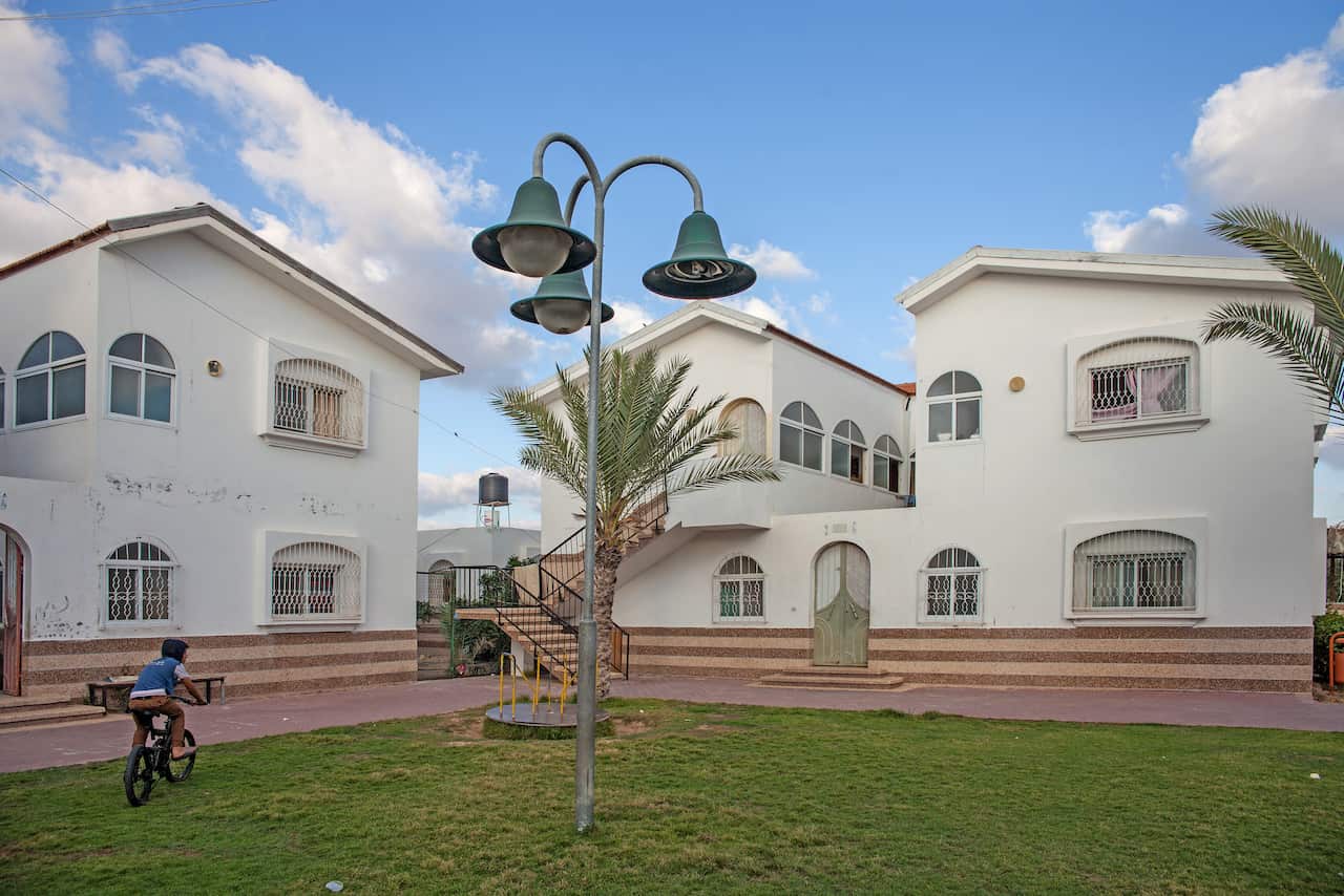 A boy rides a bike in a grassy courtyard with white buildings around it.