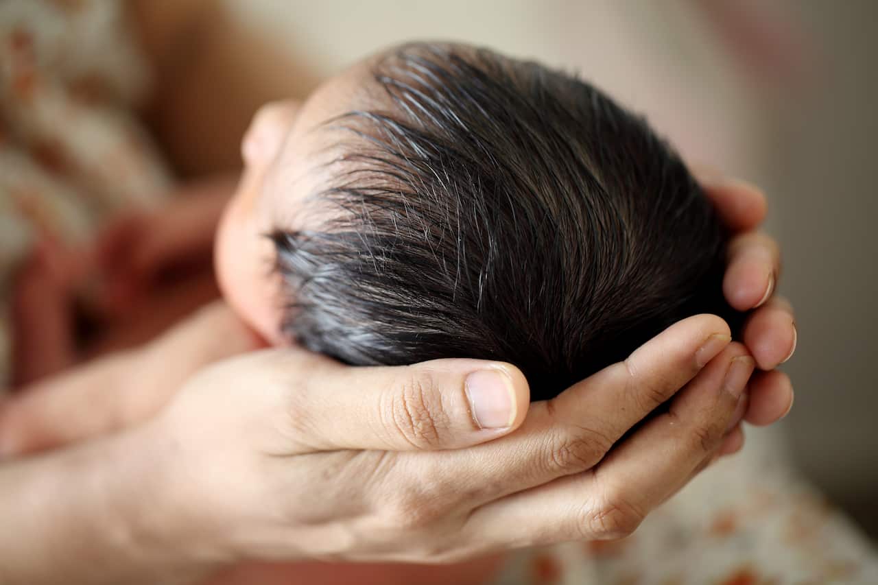 A baby's head being held in an adult's hands.