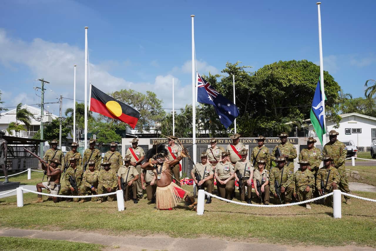 People in army uniform pose against flags.