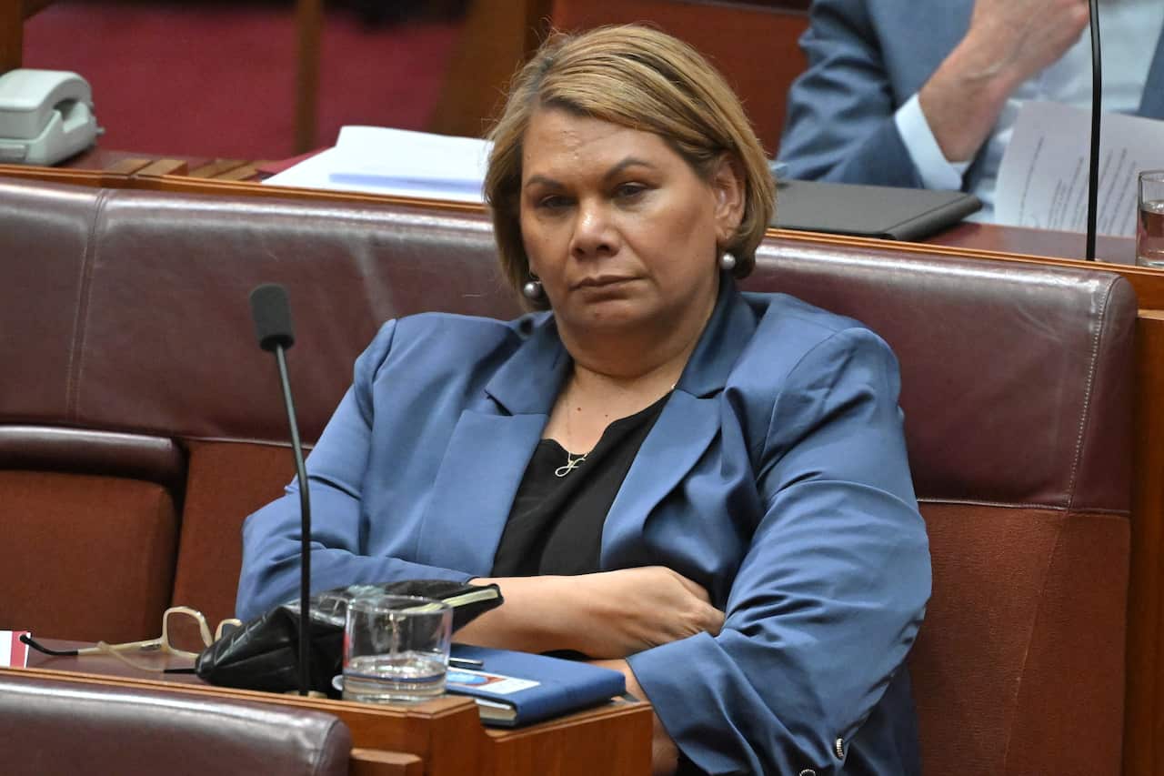 A woman in a blue blazer sitting in parliament with her arms folded.
