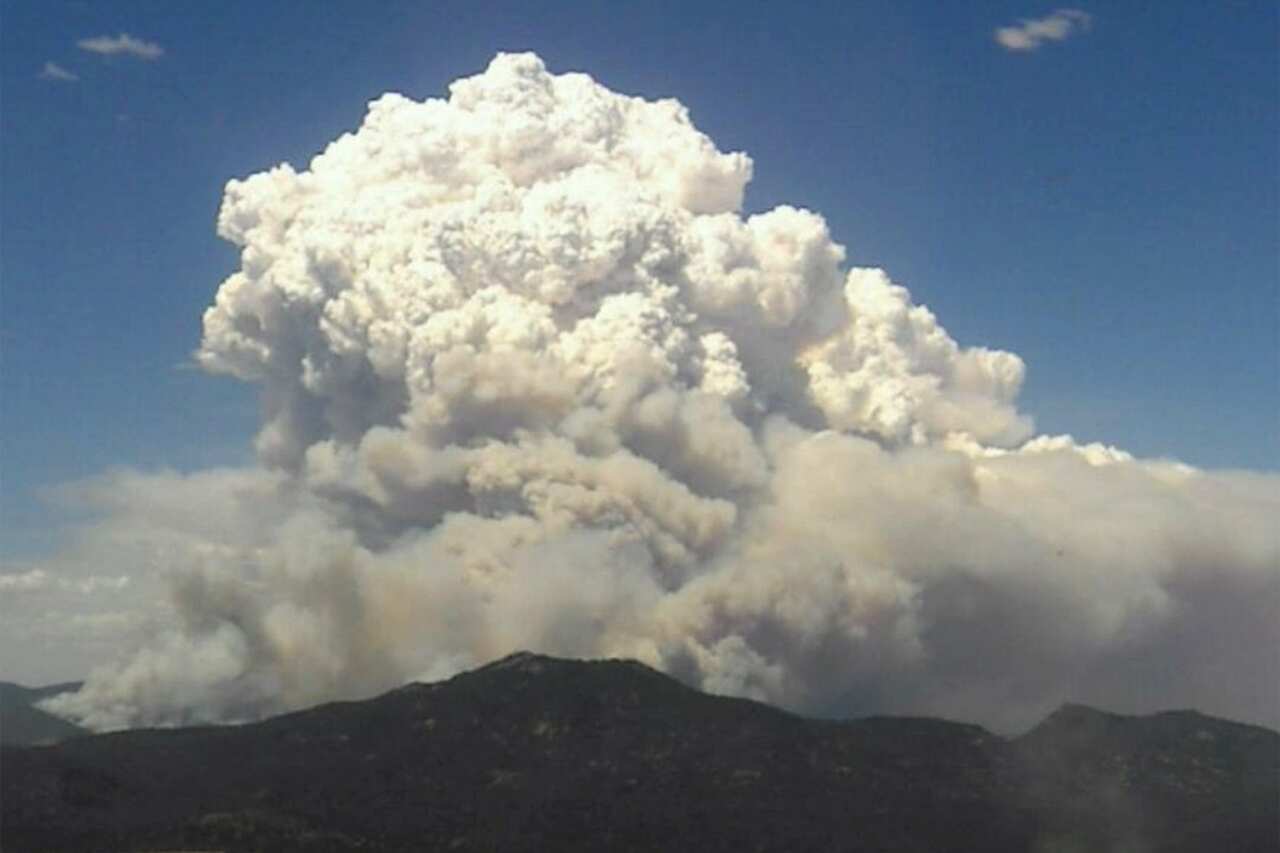 Large cloud of white and grey smoke fills the sky above mountains.