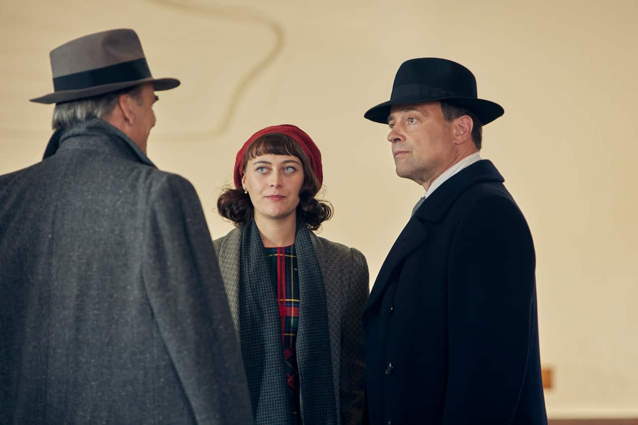 A woman and a man in 1950s era clothing stand looking at another man