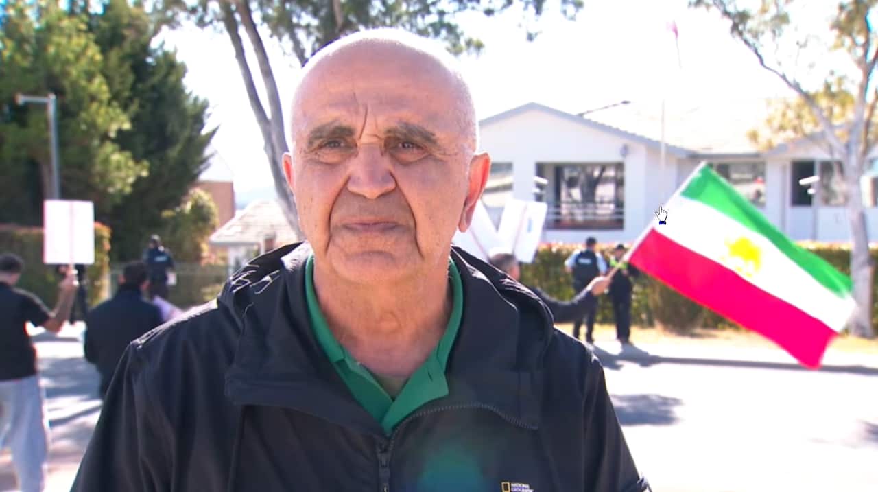 A man standing infront of an Iranian flag.
