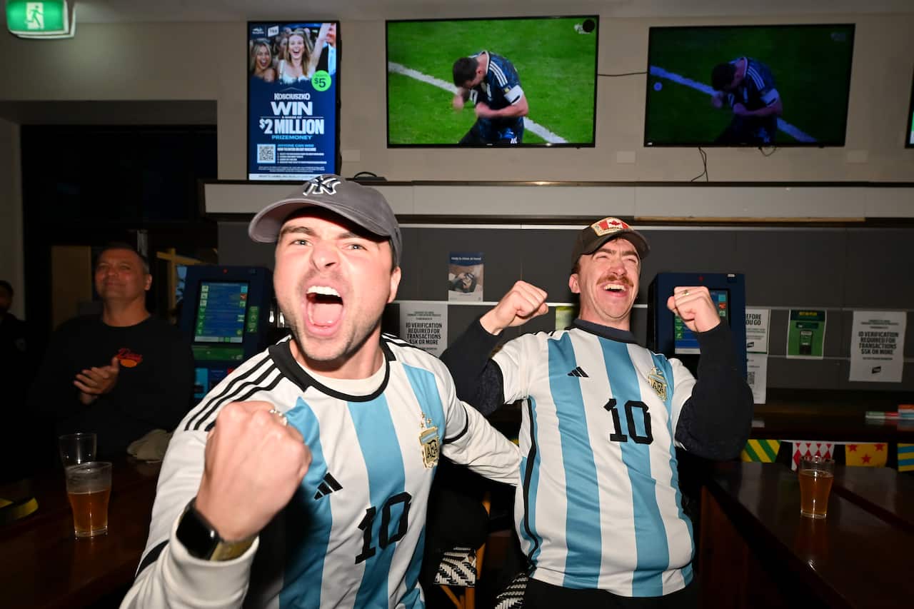 Two male football fans in Argentine jerseys celebrating at a pub