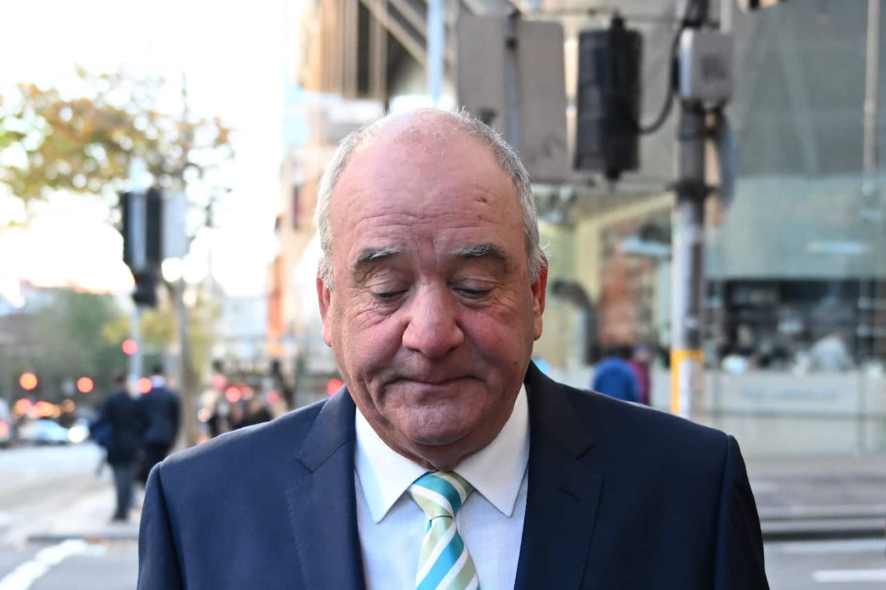 An elderly man in a blue suit and striped tie is walking down a street.