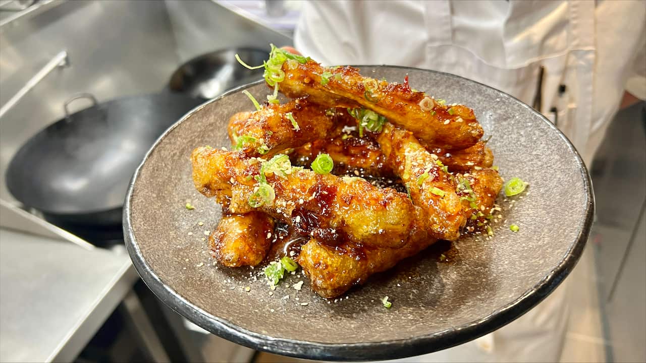 A hand holding a plate of honey chicken.