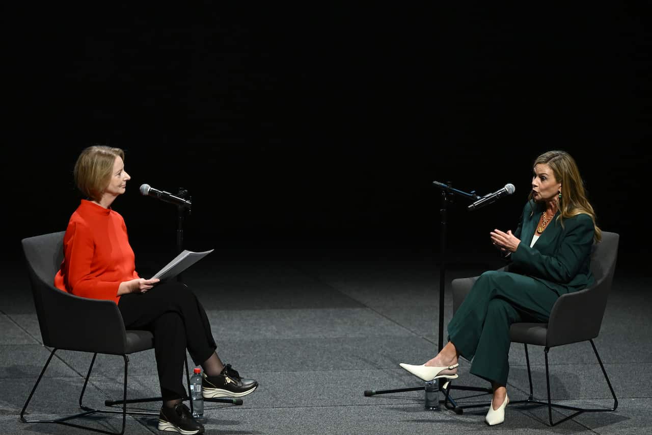 Julia Gillard sitting on a grey sofa, speaking into a microphone. Across from her is Julie Inman Grant, also sitting on a grey chair and speaking into a microphone.