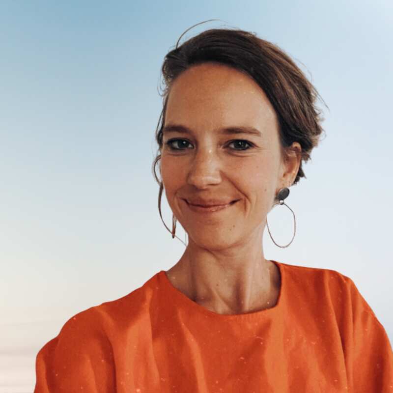 A woman wearing an orange top and hoop earrings smiles for the camera