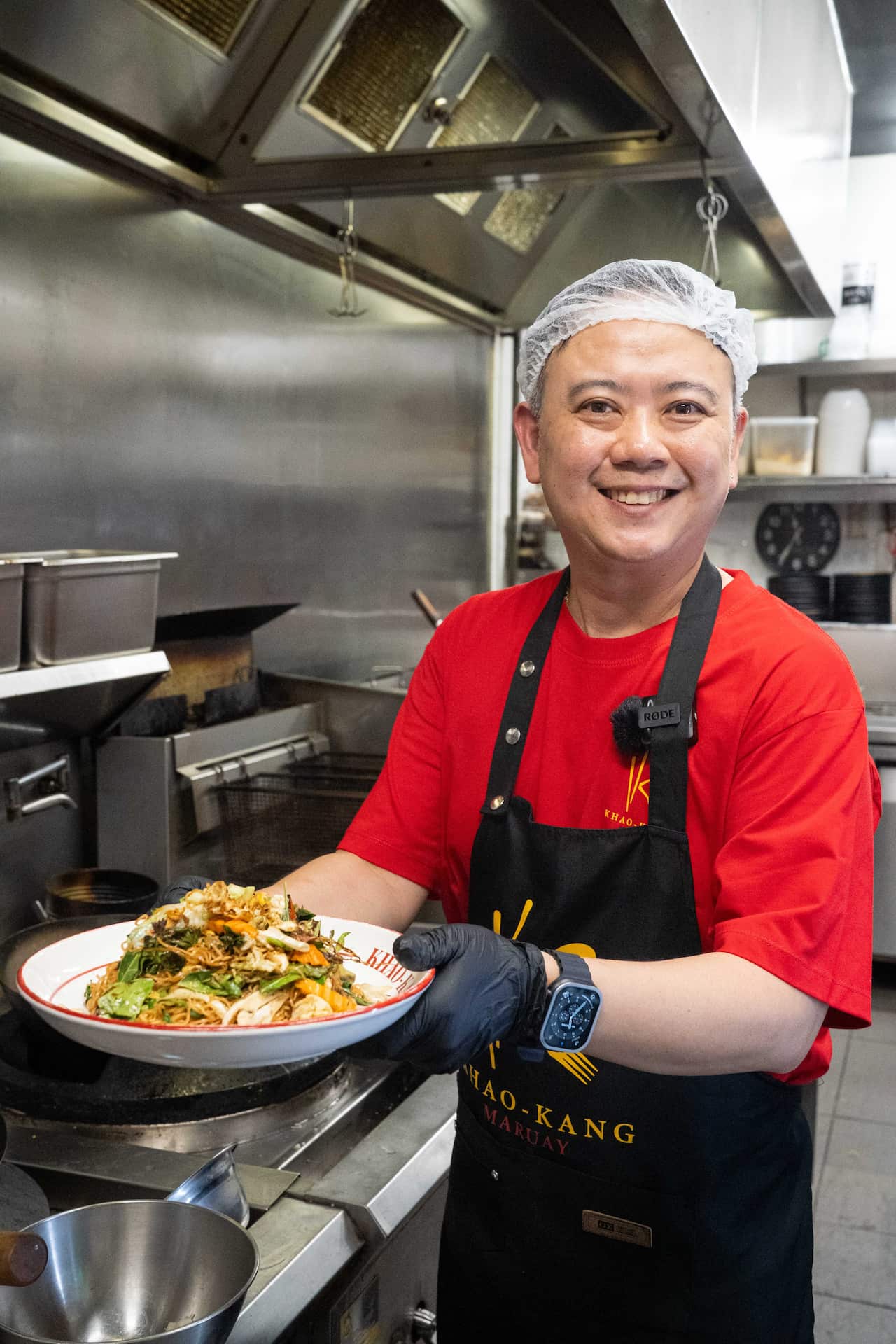 Trin from Khao Kang Maruay holding up a plate of pad kee mao mama. 