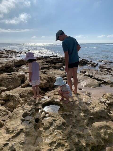 Two young girls and their father exploring rock pools by the ocean.