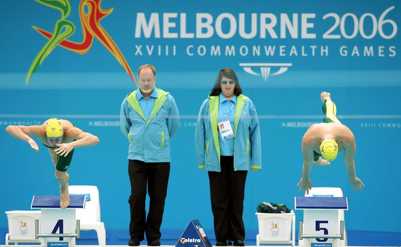 Two swimmers jump into the pool at Commonwealth Games as two match officials stand in the back.