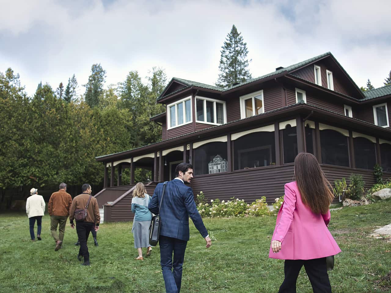 Six people walk towards a large brown country house.