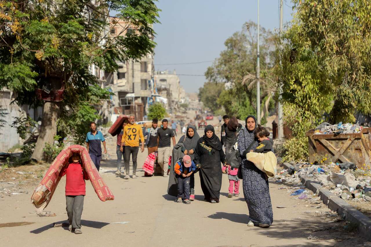 A group of people are walking, some holding bags and children. 