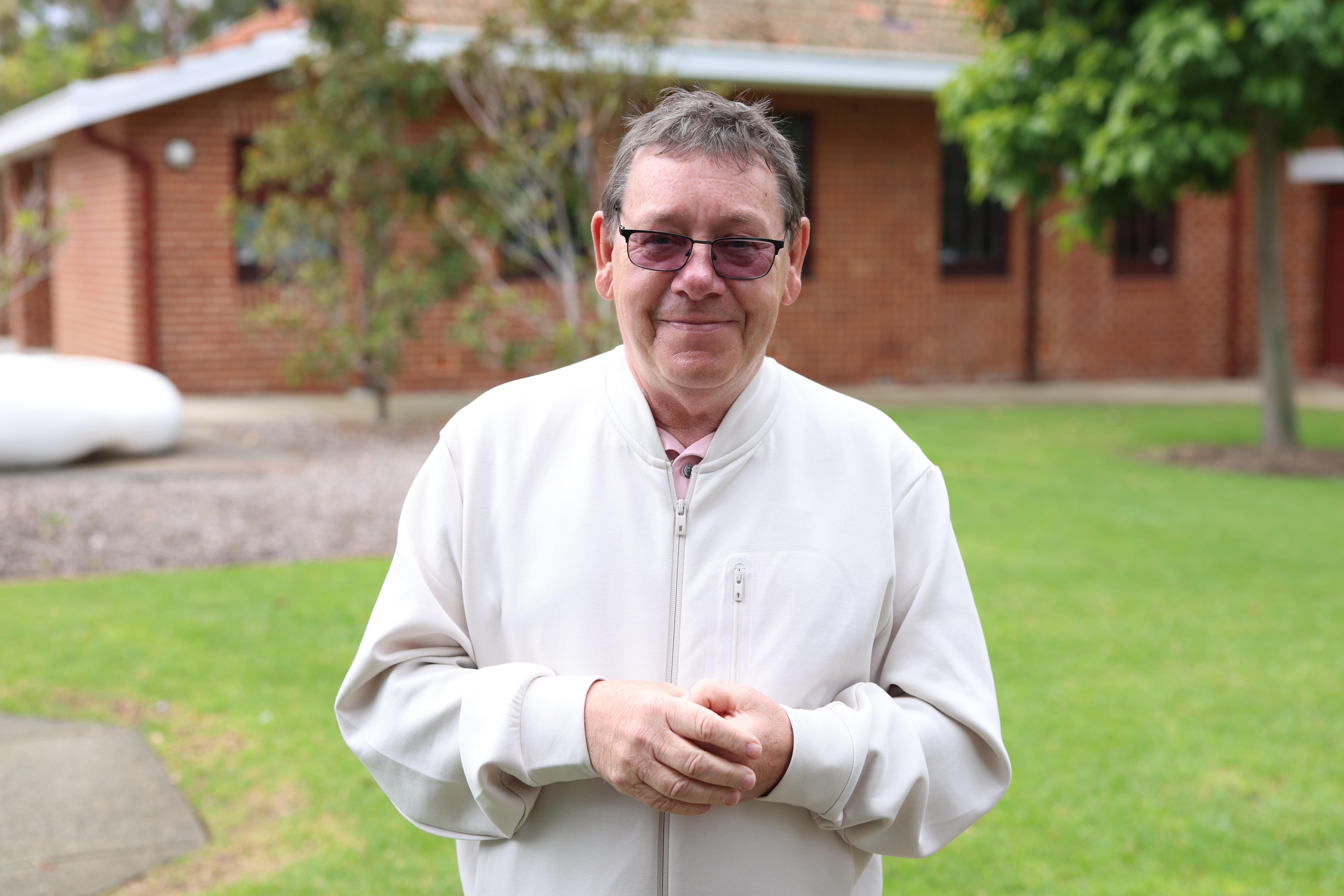 A man wearing a cream jacket stands in front of a house