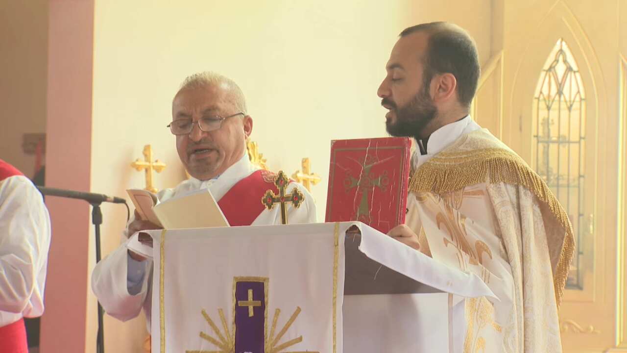 Reverend Paul Naisan (right) stands at a lectern in the Saint Zaia Cathedral.