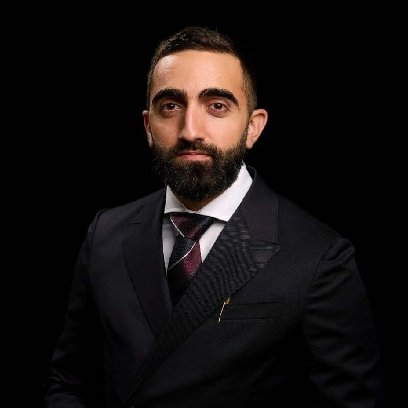 A man in a black suit in front of a black backdrop