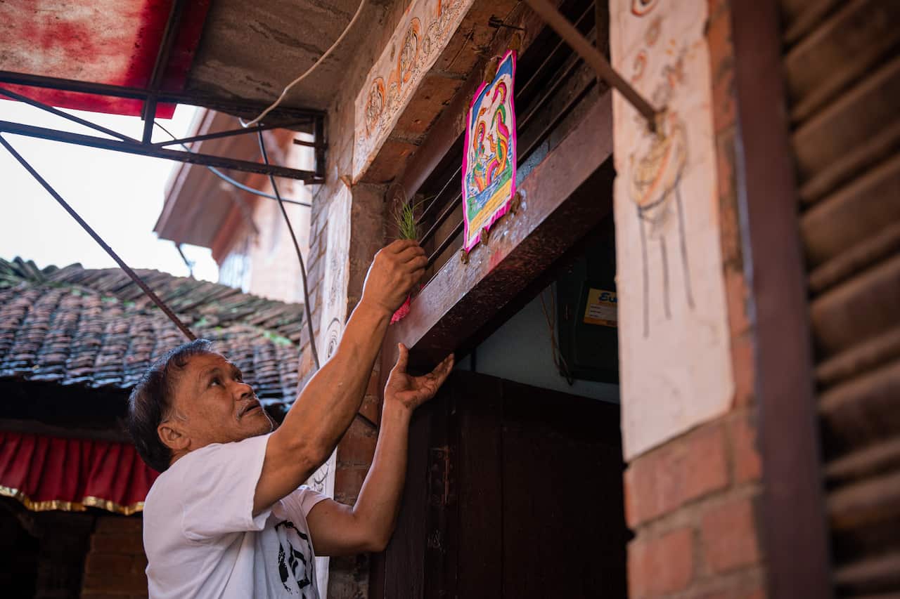 A man sticks a poster of the serpent deity (naga) above his doorstep during the Nag Panchami festival.