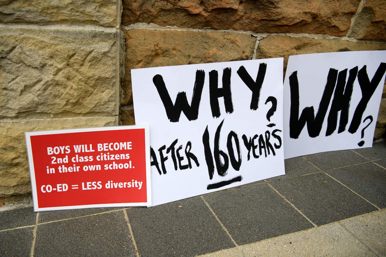 Three placards against a wall. One reads: 'Boys will become 2nd class citizens in their own school. CO-ED = LESS diversity. The others read: Why after 160 years? and Why?