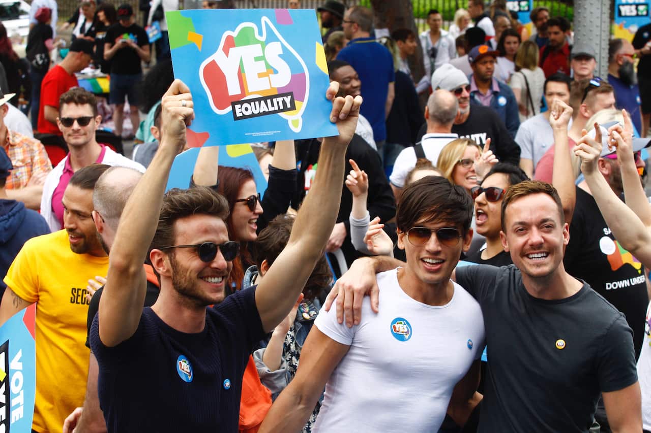 A man holds a sign that says 'YES equality', while others hug and gather around. 