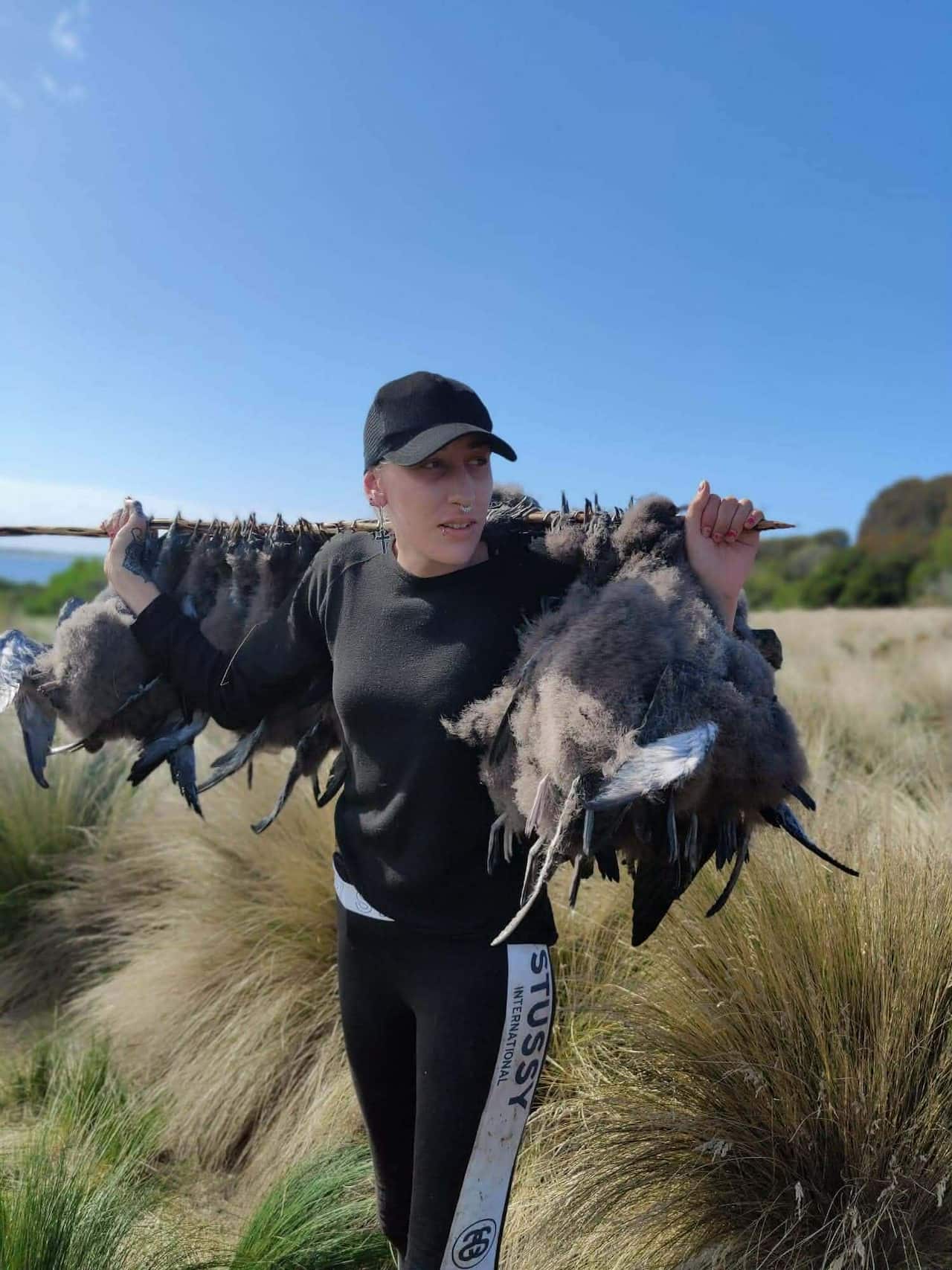 A woman holding a pole with dead birds hanging down, on her back.