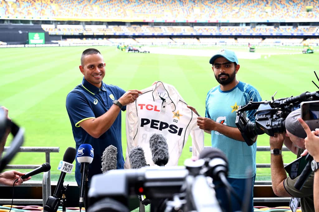 Two cricketers hold up a jersey in front of the cameras.