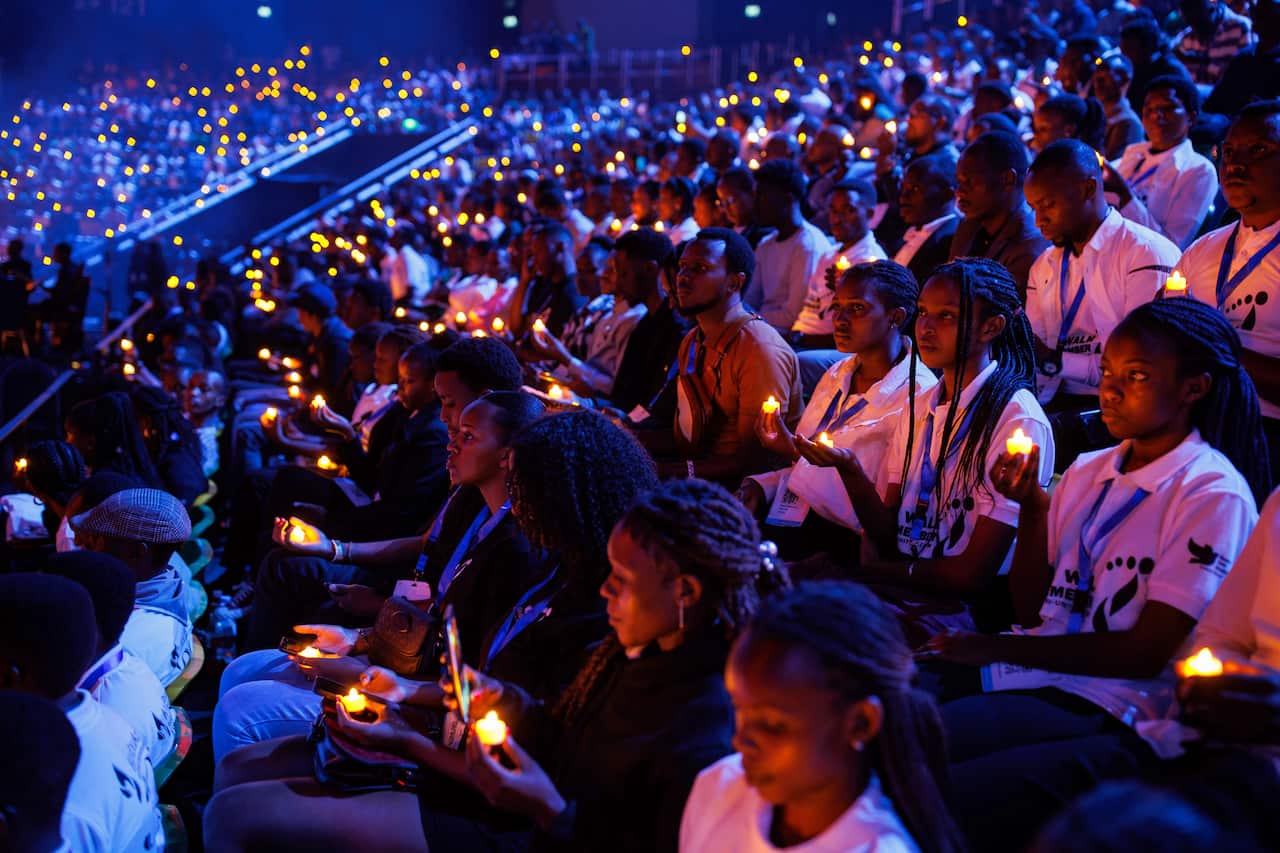 Hundreds of people hold candles in a dark stadium 