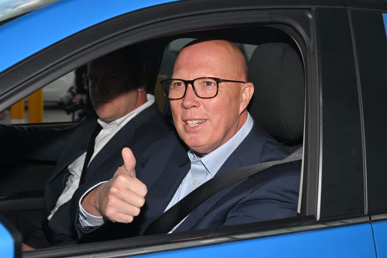 Peter Dutton sits in a car and smiles while showing a thumb up.