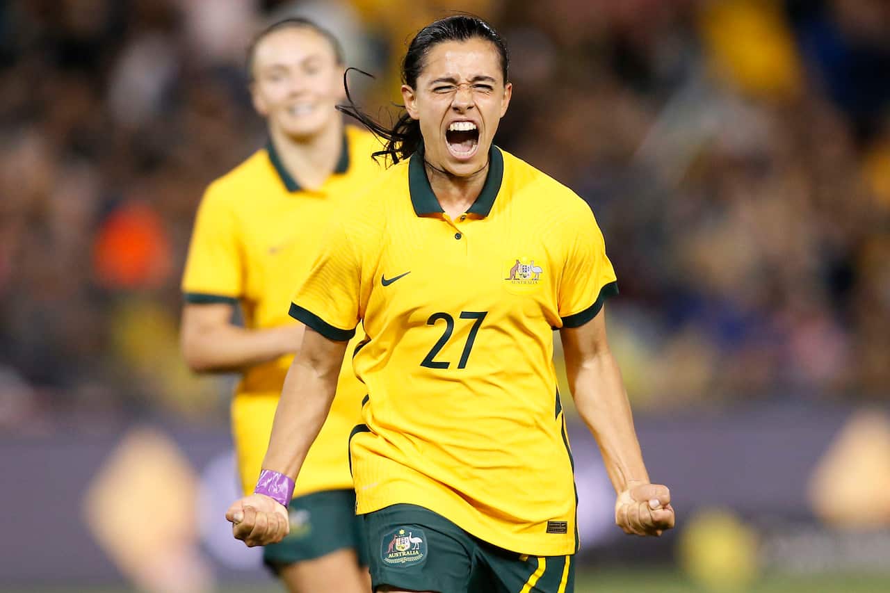 A woman in a yellow football shirt clenches both fists in celebration