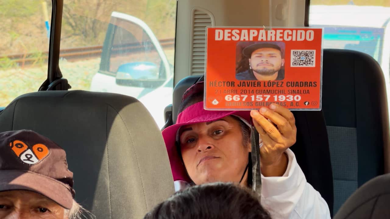 A woman in a burgundy sunhat seated inside a bus holds up a bright orange missing-person poster featuring a photograph and the Spanish word “desaparecido” at the top. The poster includes a name, date, location, QR code and contact number.