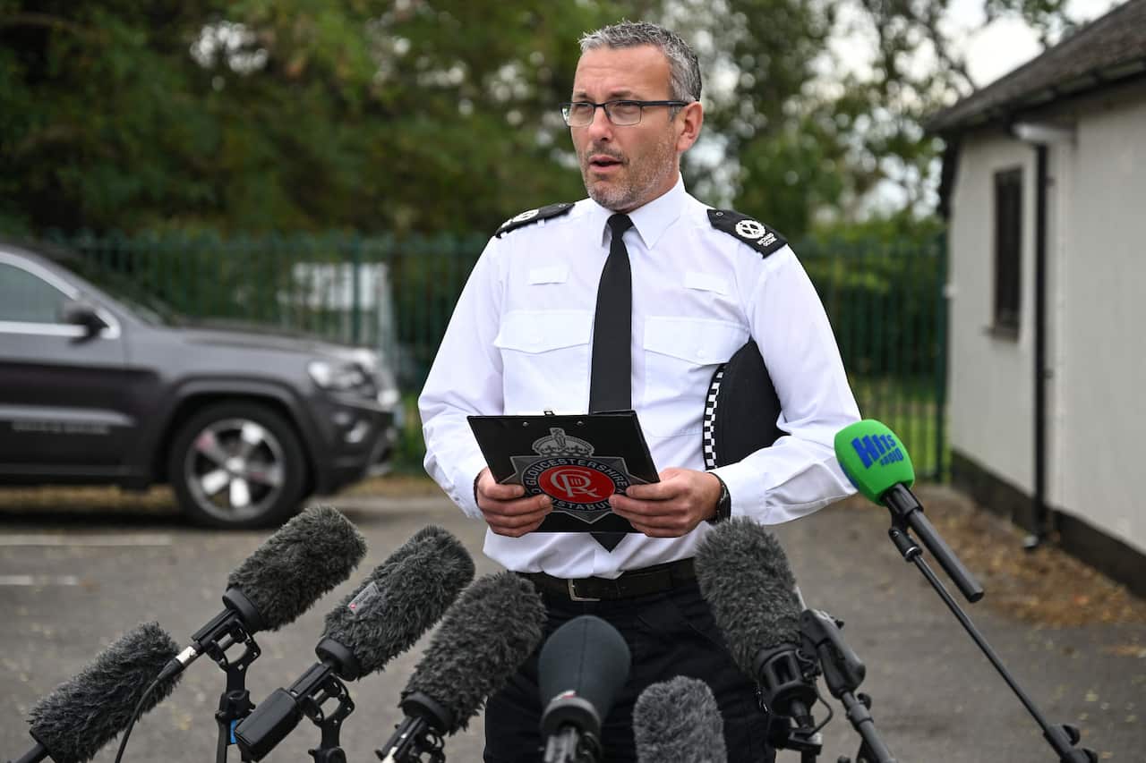 A British police officer standing in front of the media mics, talking