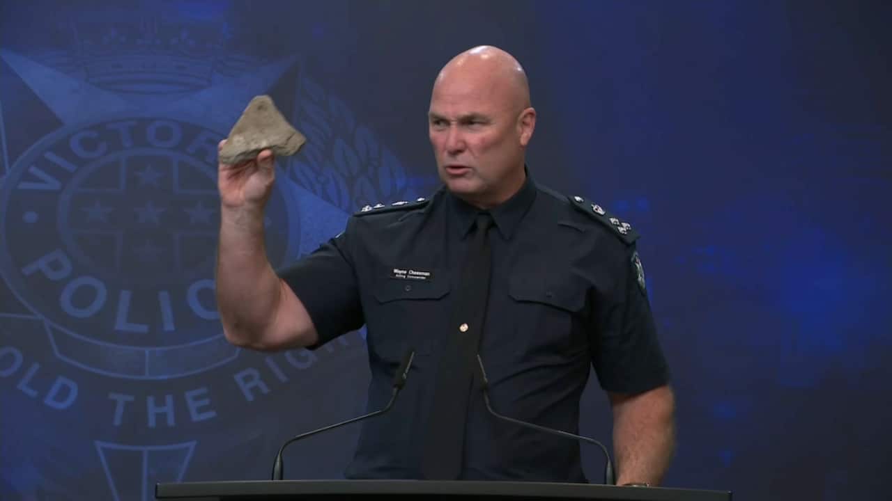 A police officer in uniform holding up a small, jagged rock at a press conference.