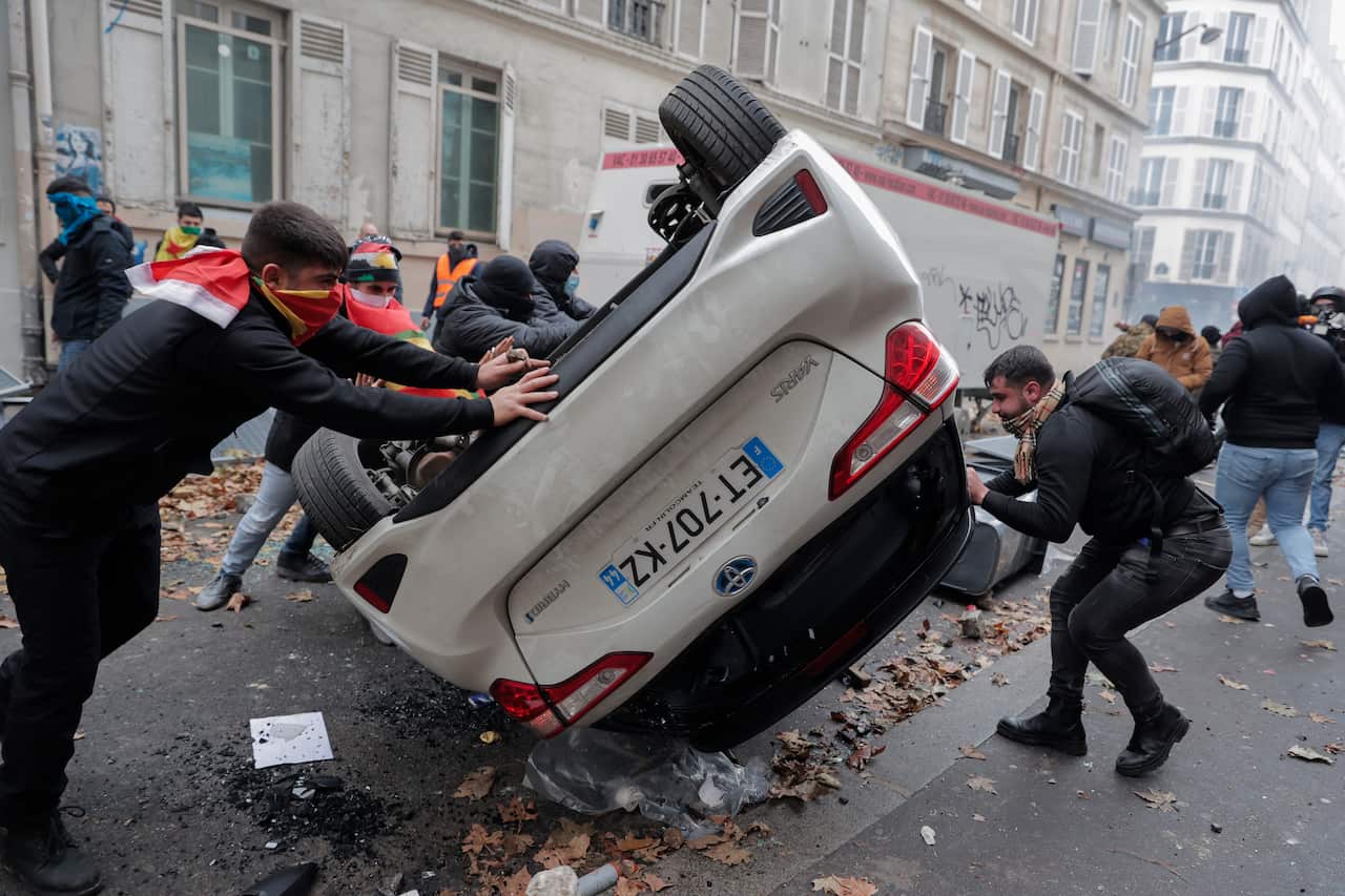 Men in a group protest by turning a car over