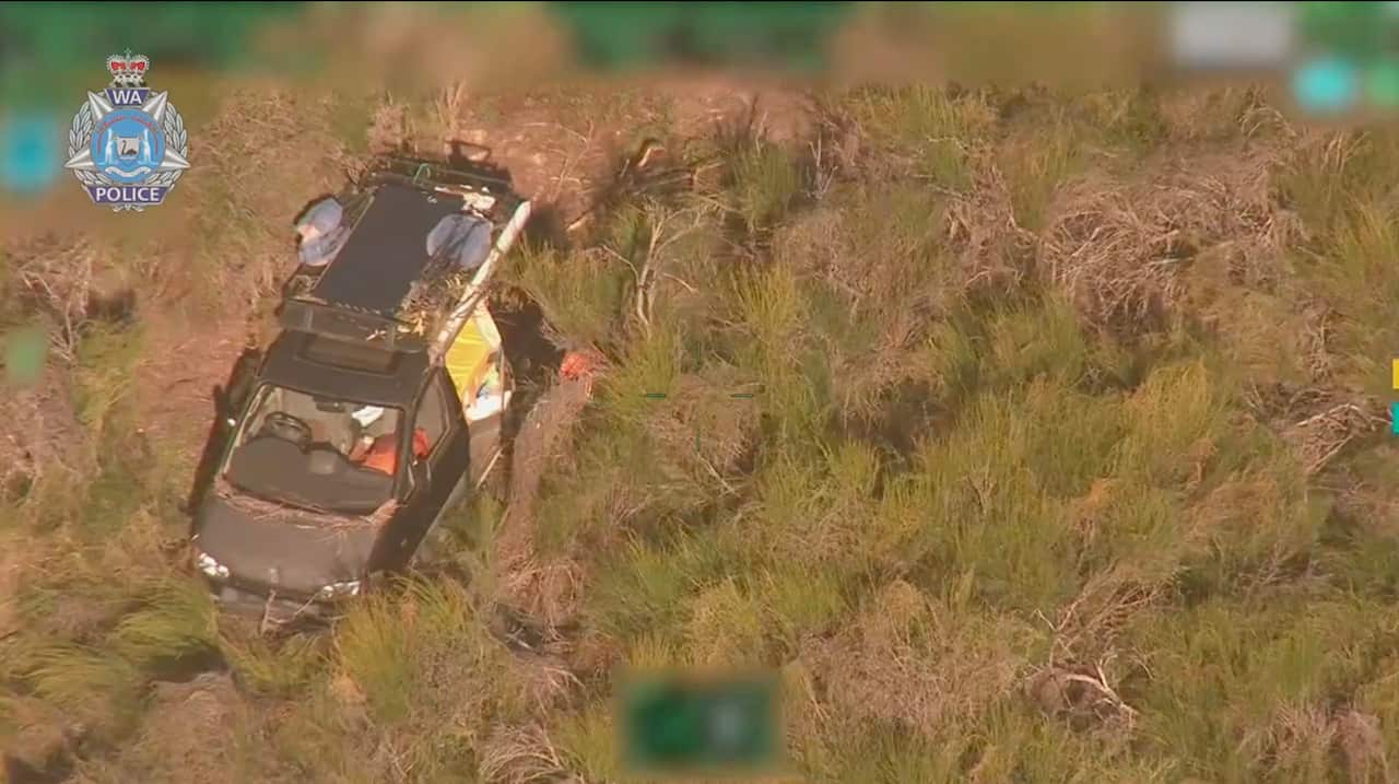 A screenshot of aerial vision of a van bogged and surrounded by rocks and scrub.