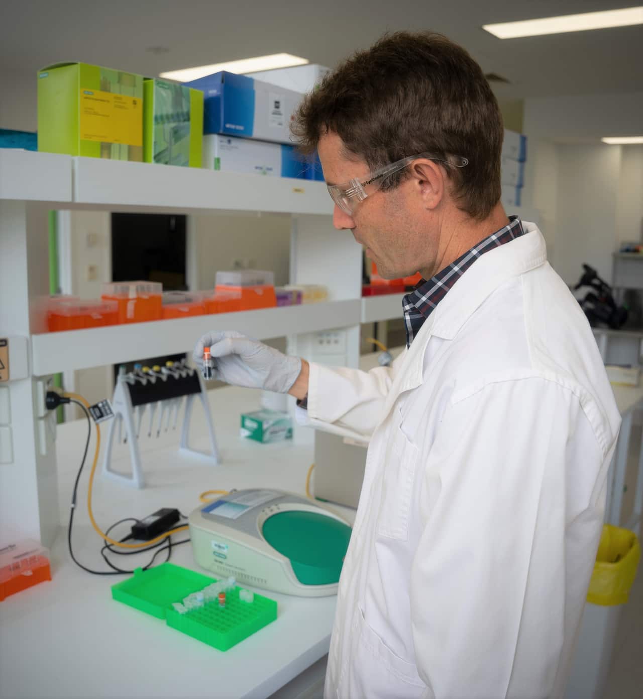 A scientist in a white lab coat stands at a laboratory table.