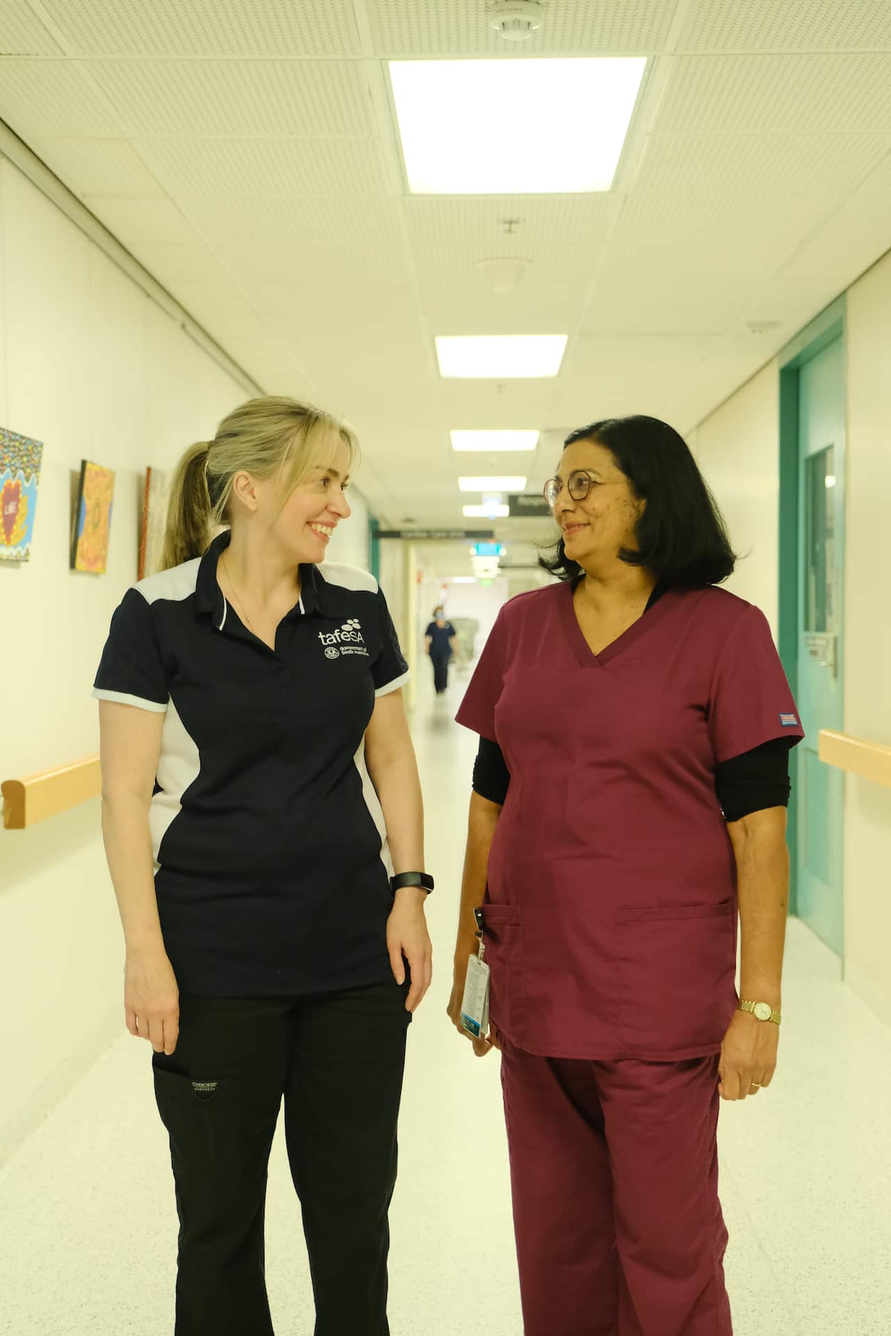 A woman in a nurse's uniform talks to another woman